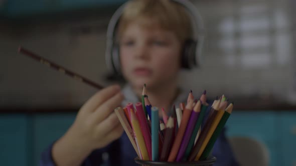 Kid in Headphones Drawing with Color Pencils Sitting Alone at Home