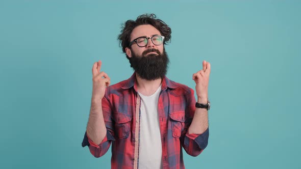 Young Man That Keeps Fingers Crossed Isolated Over Turquoise Background