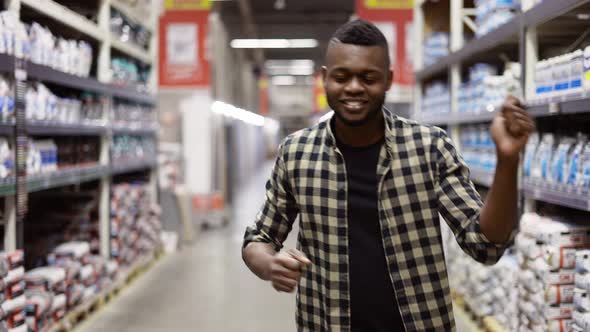 Smiling Guy Dances Gesturing in Hardware Goods Store Between Stacks Slow Motion