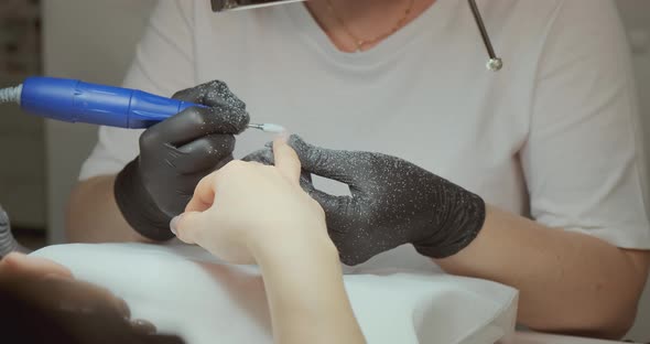 Beautician in Gloves Files Client Nails with Tool in Salon