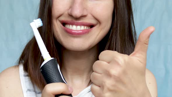 smiling young woman holding electric toothbrush and thumb up finger. good choise electric toothbrush