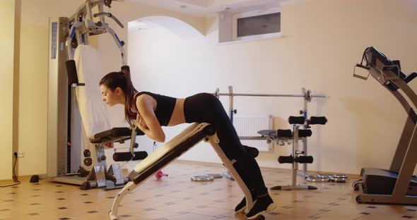 Wide Shot Side View of Slender Young Woman Training on Exercise Bench in Gym