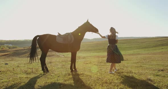 Girl Walking with Horse Among Meadows with Sun Shining and Caressing It