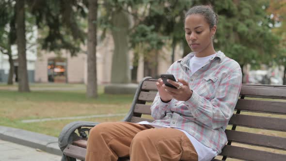 African Woman Using Smartphone While Sitting Outdoor on Bench