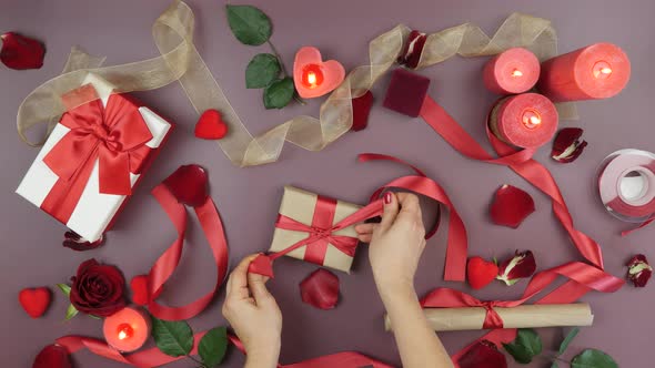 Hands are wrapping gift box with craft paper and red ribbon for St. Valentine's Day