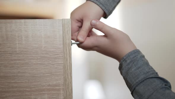 Child Unscrews Screw From Chipboard of Furniture Panel with Hex Key Closeup