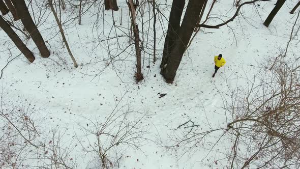 Male Runner in Yellow Coat Training in Forest on Winter Day