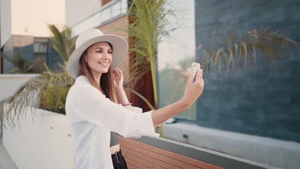 Happy Young Woman in Stylish Clothes and Hat Taking Selfie on Modern Smartphone