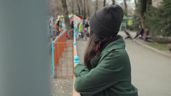 Lonely Young Woman Dressed in a Green Coat in the Park