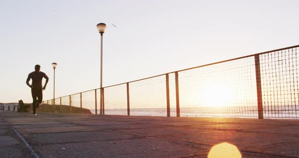 Focused african american man running exercising outdoors by seaside at sunset