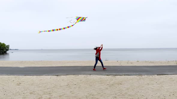 Aero, Woman Flies a Bright, Colorful Rainbow Kite Into the Sky on the Beach, Nice Weather, Spring