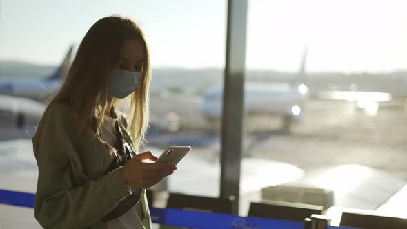 Blonde Woman in Medical Mask Uses Phone Walking Through Airport Terminal