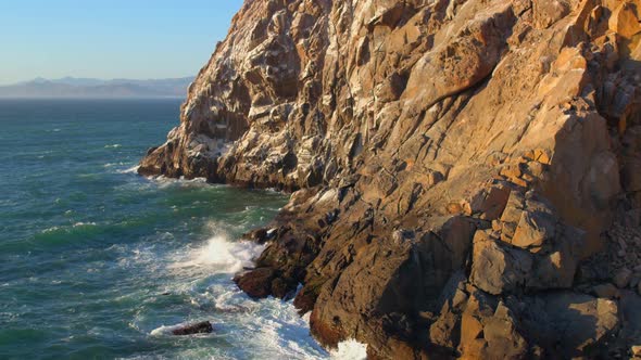 Forward Pan of Waves Crashing on Morro Rock California on a Sunny Day