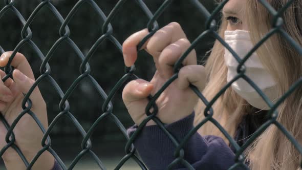 Closed Border. Quarantine. Close-up of Young Woman Wearing Protective Face Mask Stand Behind Fence