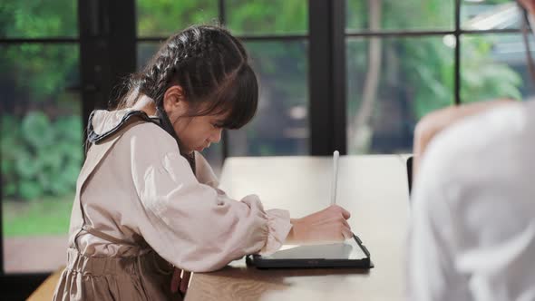 Homeschool Asian little young girl learning online class  with mother work from home behind. alt