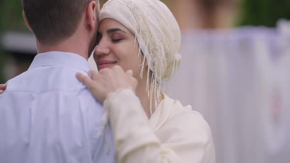 Portrait of Happy Charming Middle Eastern Bride in Hijab Hugging Unrecognizable Groom Looking at