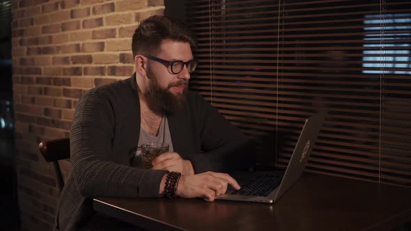 Man Is Enjoying Beverage in a Bar in Evening Taking Video Call By His Laptop