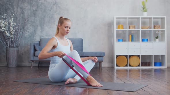 Young and sporty girl in sportswear is using resistance band while doing at home.