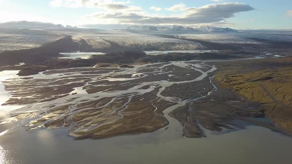 Aerial dolly out of fiords and lake in lowlands, Breiðamerkurjökull glacier in background on a cloud