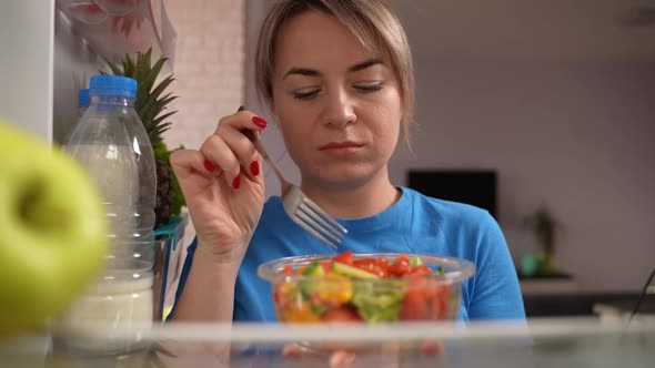 Slimming Woman Eating Tasteless Salad at Fridge