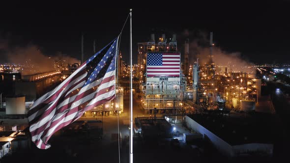 Waving Flag of United States Against the Background of Petroleum Refinery at Night alt