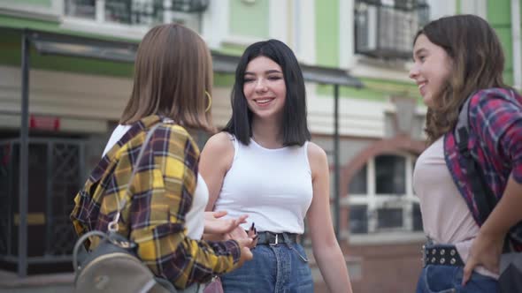 Positive Caucasian Teenage Girls Standing on City Street Talking Laughing