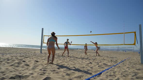 Women players play beach volleyball and a player digs the ball.