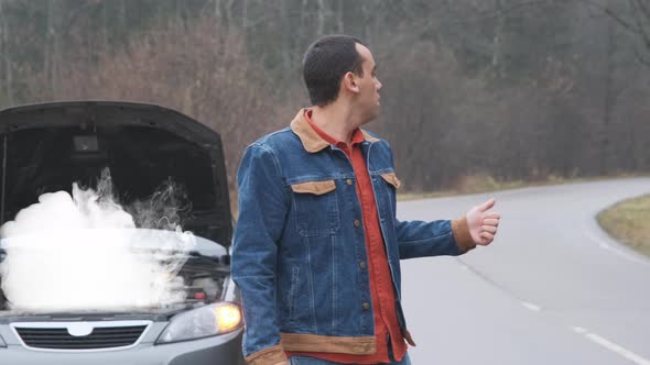 Young Man Hitchhiking on a Road with His Broken Down Car