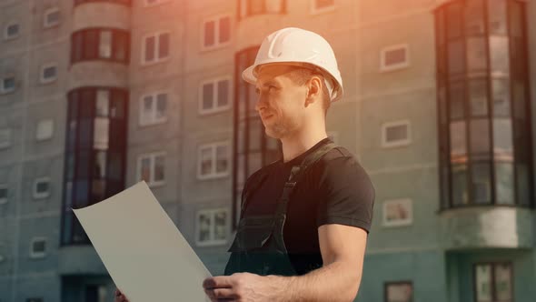 A Man in a Helmet Is Holding a Construction Plan in His Hands. A Builder Is Checking Blueprints.