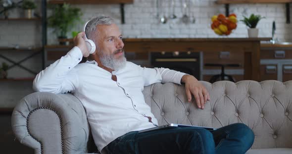 Portrait of Mature Bearded Man with Grey Hair Enjoying Listening Music with Wireless Headphones and