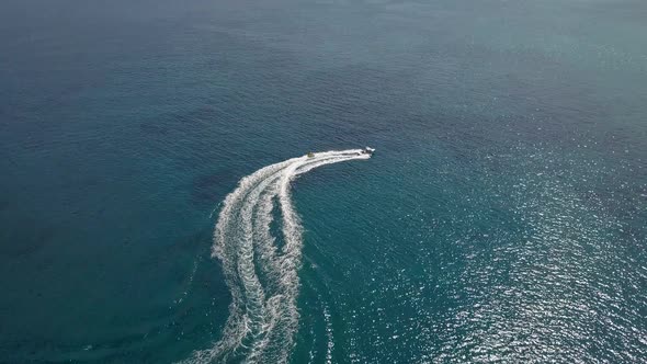 Drone shot from above a speedboat pulling a passenger on a tube in the Aegean Sea; Paros island, Gre