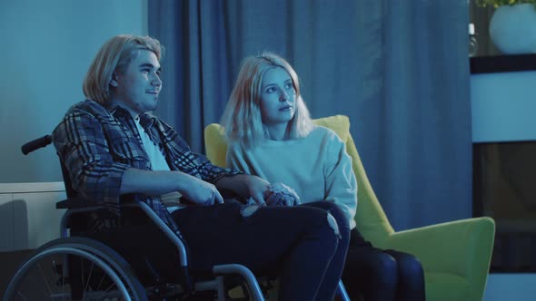 Young Couple of Young Woman and Man in a Wheelchair Watching TV