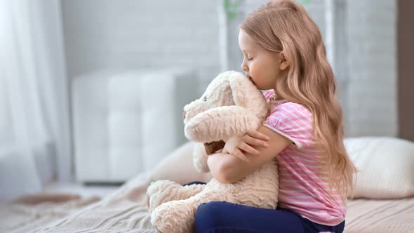 Pensive Little Girl Upset Hug Toy Teddy Sitting on Bed at Comfortable Bedroom