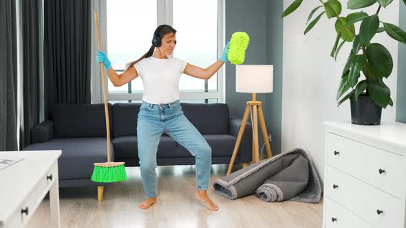 Woman in Headphones Cleaning the House and Having Fun Dancing with a Broom and Washcloth