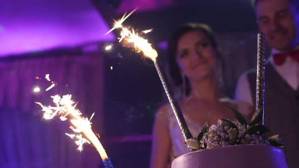 Sparklers on the wedding cake, bride and groom in the background