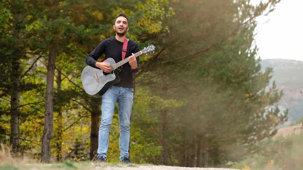 Young Man Plays On Guitar And Sings In The Forest