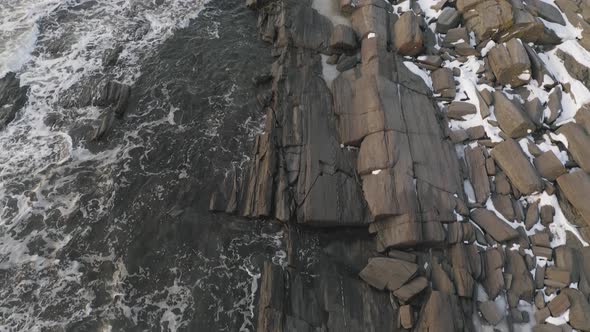 Tilt up as waves lap the rocky shore, winter sunrise AERIAL