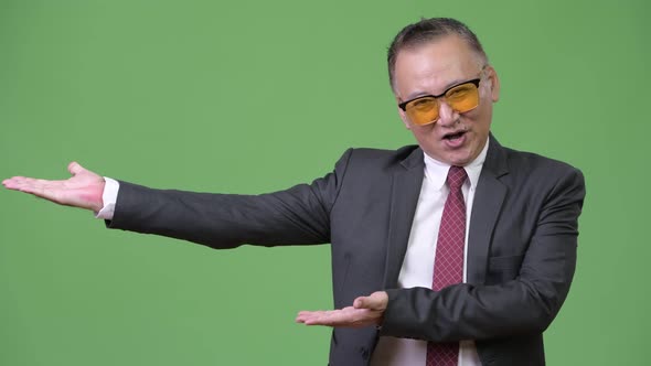 Mature Japanese Businessman Wearing Sunglasses Against Green Background