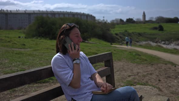 The Girl Talks on the Phone Sitting on a Bench and Looking at the Sea