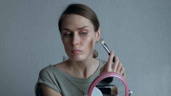 Woman Doing Makeup on Face in Front of a Round Mirror