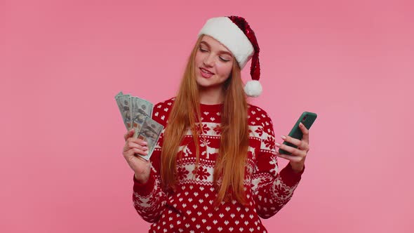 Girl in Red Christmas Sweater Using Mobile Phone Hold Money Dollar Cash Doing Online Gift Shopping