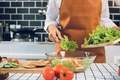 Asian woman is using tongs to take the salad on the wooden cutting board onto the salad cup in the k - PhotoDune Item for Sale