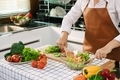 Asian woman is mixing the ingredients in a salad bowl at the kitchen cooking table. - PhotoDune Item for Sale