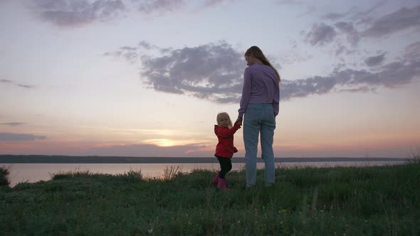 Cinematic Portrait of Young Mother and Her Little Daughter at Sunset on Field Near Seashore Slow