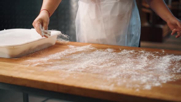 The cook sprinkles the table with flour before working with the dough