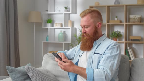 Addicted to Technology Young Handsome Redhead Man Resting on Cozy Sofa Involved in Using Smartphone