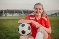 Portrait of smiling girl football player with soccer ball sitting on the grass - PhotoDune Item for Sale