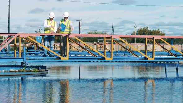 Two Male Specialists Discussing a Large Round Sedimentation Tank