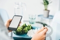 Woman Using Smart Phone While Eating Broccoli and rice at home.  - PhotoDune Item for Sale