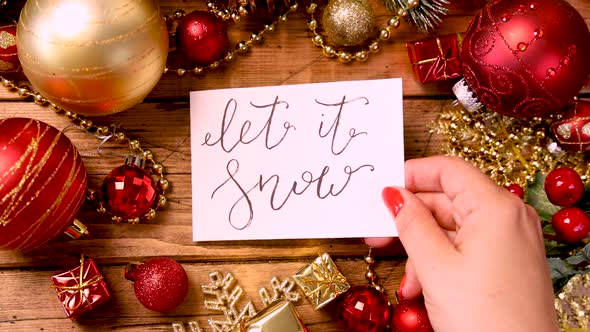 Hands bringing a Christmas card with text LET IT SNOW close to camera